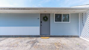 A single-story house with a gray door, a number 16 on the door, a small window with a white lattice, and a concrete driveway. - COZY, BEAUTIFUL APARTMENT AT AVANTI COVE (Conneaut Lake)