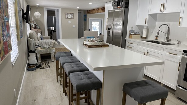 Une cuisine moderne dotée d’un grand îlot central, de tabourets en bois, de meubles blancs et d’appareils électroménagers en acier inoxydable.