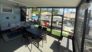 Une terrasse couverte avec une table et des chaises, un canapé et une vue sur une piscine et des bateaux.