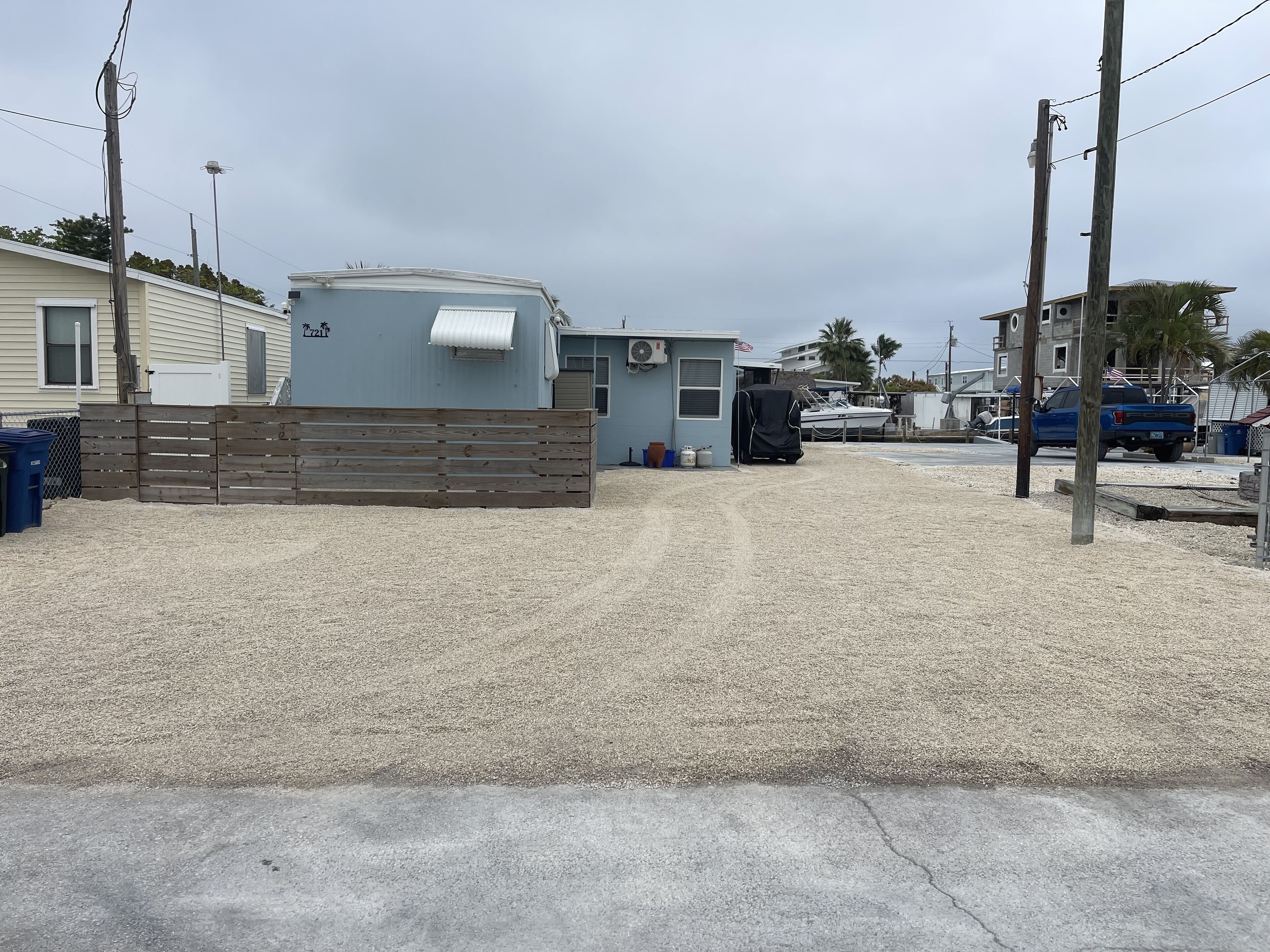 A residential area with a trailer, a small building with an American flag, and a blue truck.