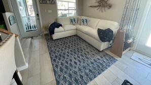 Un salon avec un canapé blanc, un tapis à motifs bleus, un ventilateur de plafond et un panneau mural sur lequel on peut lire : « Bienvenue à CASA TATA ».