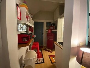Une cuisine étroite avec des appareils électroménagers rouges, un évier blanc et un petit coin repas agrémenté d’une chaise rouge.