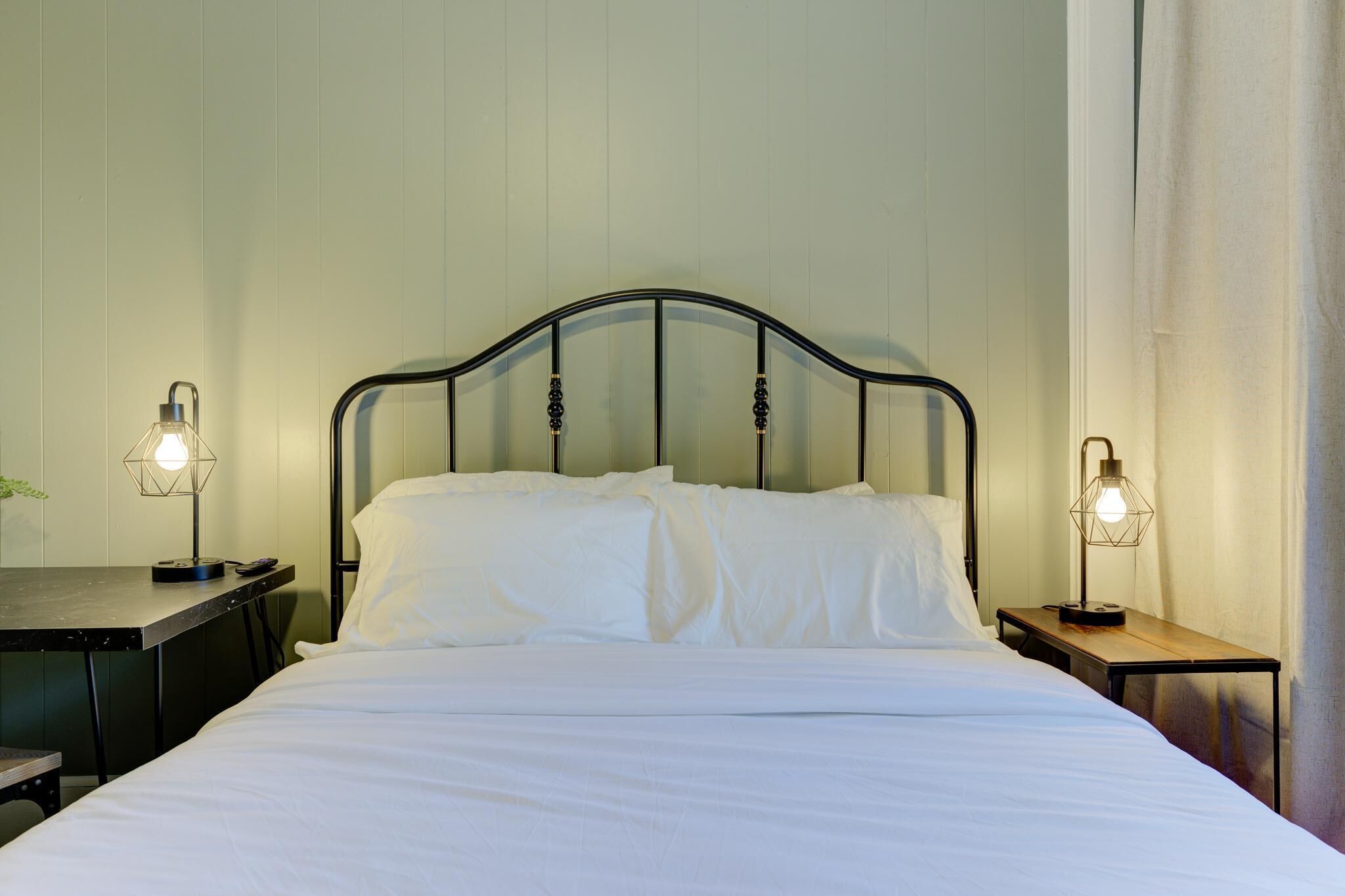 A neatly made bed with white linens, a metal headboard, and two bedside tables with lamps.