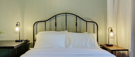 A neatly made bed with white linens, a metal headboard, and two bedside tables with lamps.