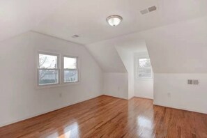 Loft-style apartment with a sloped ceiling and large window, featuring a polished wood floor and clean lines.