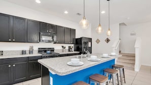 A modern kitchen with dark cabinets, a blue island, and bar stools. - Private Views & Theme Rooms, Perfect for Families! (Davenport)