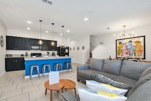 A modern kitchen with black cabinets, a blue island, and bar stools. There is a gray sofa and a small wooden table with two stools. - Private Views & Theme Rooms, Perfect for Families! (Davenport)