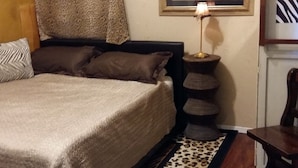 Un dormitorio con una cama, una mesita de noche, una lámpara, un cuadro enmarcado y una alfombra estampada de cebra.