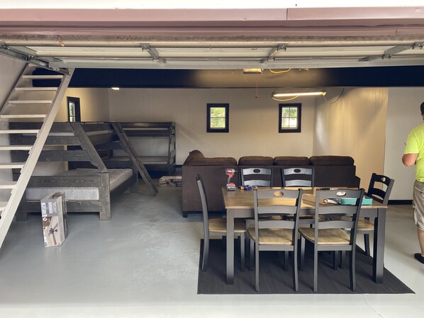 Una habitación con literas, una mesa de comedor con sillas y una escalera.