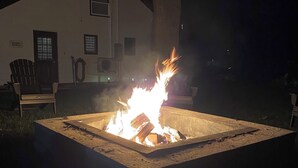 A square fire pit with burning logs in a backyard at night.