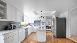 A modern kitchen with white cabinetry, a central island, and a stainless steel refrigerator. - Black Oak by Avantstay Modern & Chic Santa Rosa Hideaway With Pool Table, & Fire Pit (Santa Rosa)