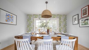 A dining area with a wooden table, white chairs, and a hanging woven light fixture. - Black Oak by Avantstay Modern & Chic Santa Rosa Hideaway With Pool Table, & Fire Pit (Santa Rosa)