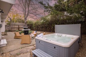 A backyard with a hot tub, wicker furniture, and a barbecue grill.