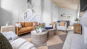 A spacious living room with a staircase, a sofa, two round wicker ottomans, and a coffee table. - Black Oak by Avantstay Modern & Chic Santa Rosa Hideaway With Pool Table, & Fire Pit (Santa Rosa)