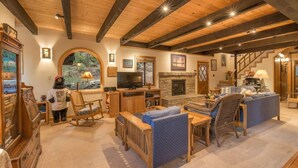 A cozy living room with wooden beams, a fireplace, a television, and comfortable seating. - Musketeer by Avantstay Family Friendly Home In Tahoe Swiss Village! (Homewood)