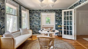 A room with a sofa, a round table with drinks, a wicker chair, and a door with glass panels. - Crawdad by Avantstay Isle of Palms Home w/ BBQ (Isle of Palms)