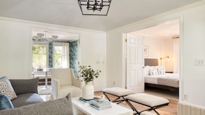 A modern living room with a sofa, coffee table, and ottoman, a dining area with a table and chairs, and a bedroom with a bed and nightstand. - Crawdad by Avantstay Isle of Palms Home w/ BBQ (Isle of Palms)