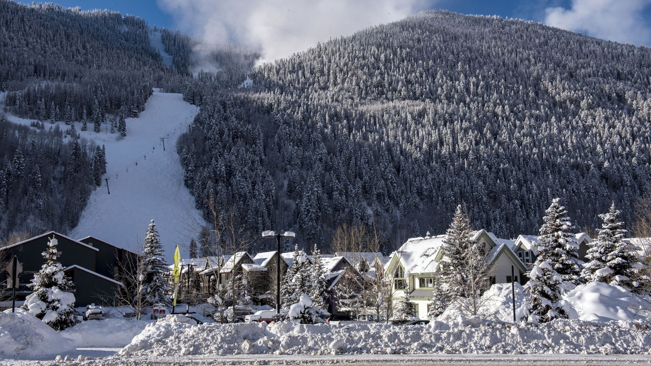 Una montaña nevada con una pista de esquí, casas con tejados cubiertos de nieve y un cielo despejado.