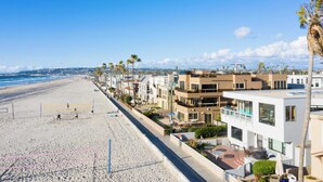 Un hotel frente a la playa con arquitectura moderna, una playa de arena y un cielo azul despejado.