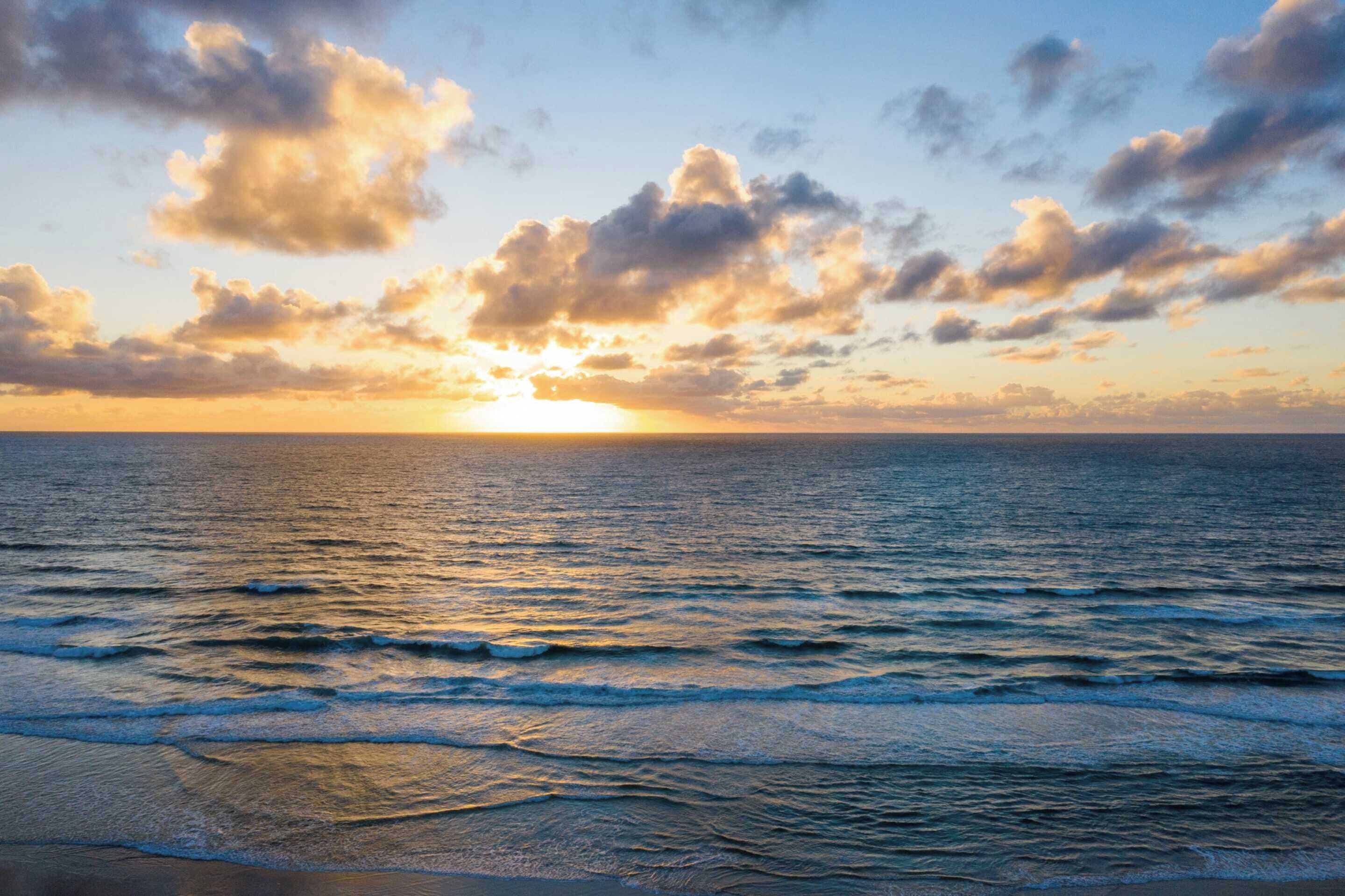A sunset over the ocean with waves and clouds.