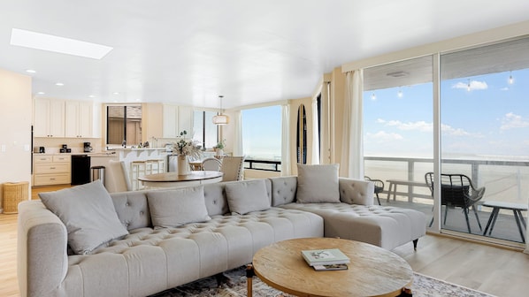 A modern living room with a sectional sofa, a round coffee table, and a view of the beach through large windows. - Beachfront Home w/ Ocean Views Right on Mission Beach Belmont by Avantstay (San Diego)
