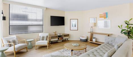 A living room with a sofa, chairs, a coffee table, a TV, and a bookshelf.