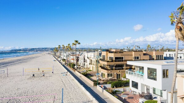 A beachfront hotel with modern architecture, a sandy beach, and a clear blue sky.