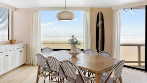 Un comedor con vista a la playa, una tabla de surf y una lámpara colgante.