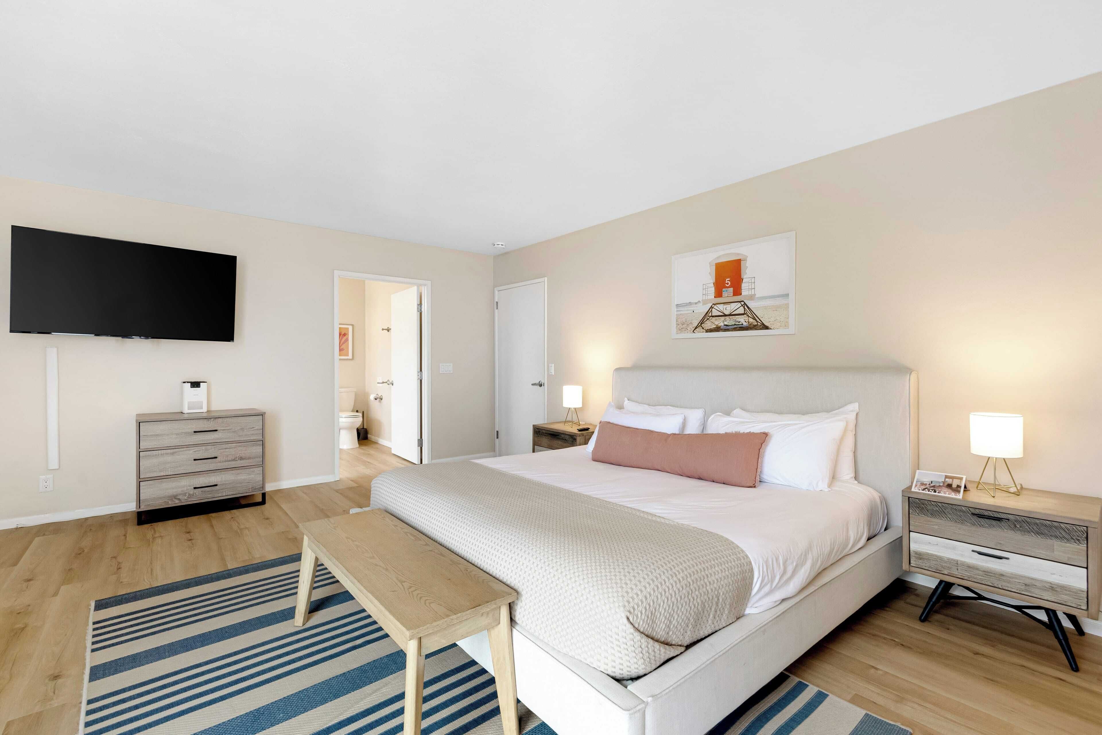 A modern bedroom with a large bed, bedside tables, a flat-screen TV, and a painting on the wall.