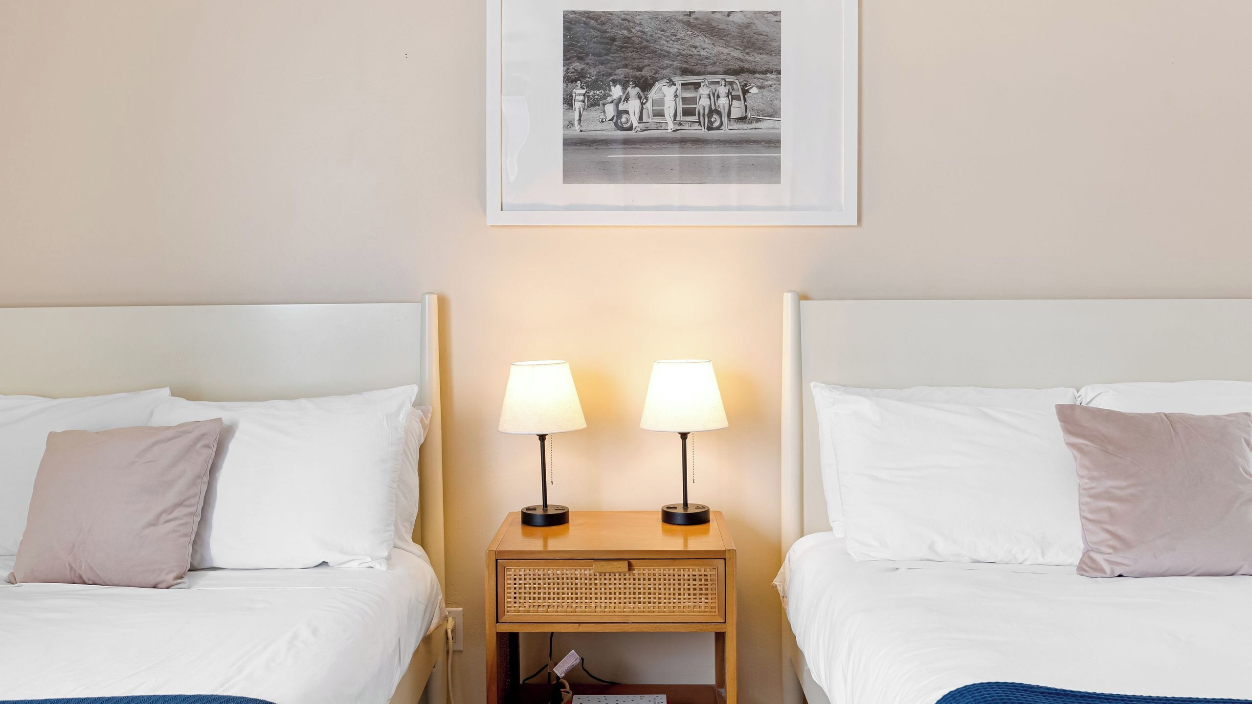 A hotel room with two beds, a framed picture on the wall, and two bedside lamps.