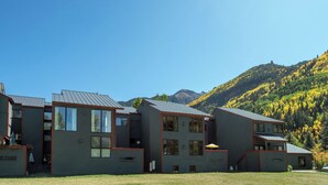 Un edificio moderno a più piani con ampie finestre e tetto piatto, circondato da un'area verde con montagne sullo sfondo.