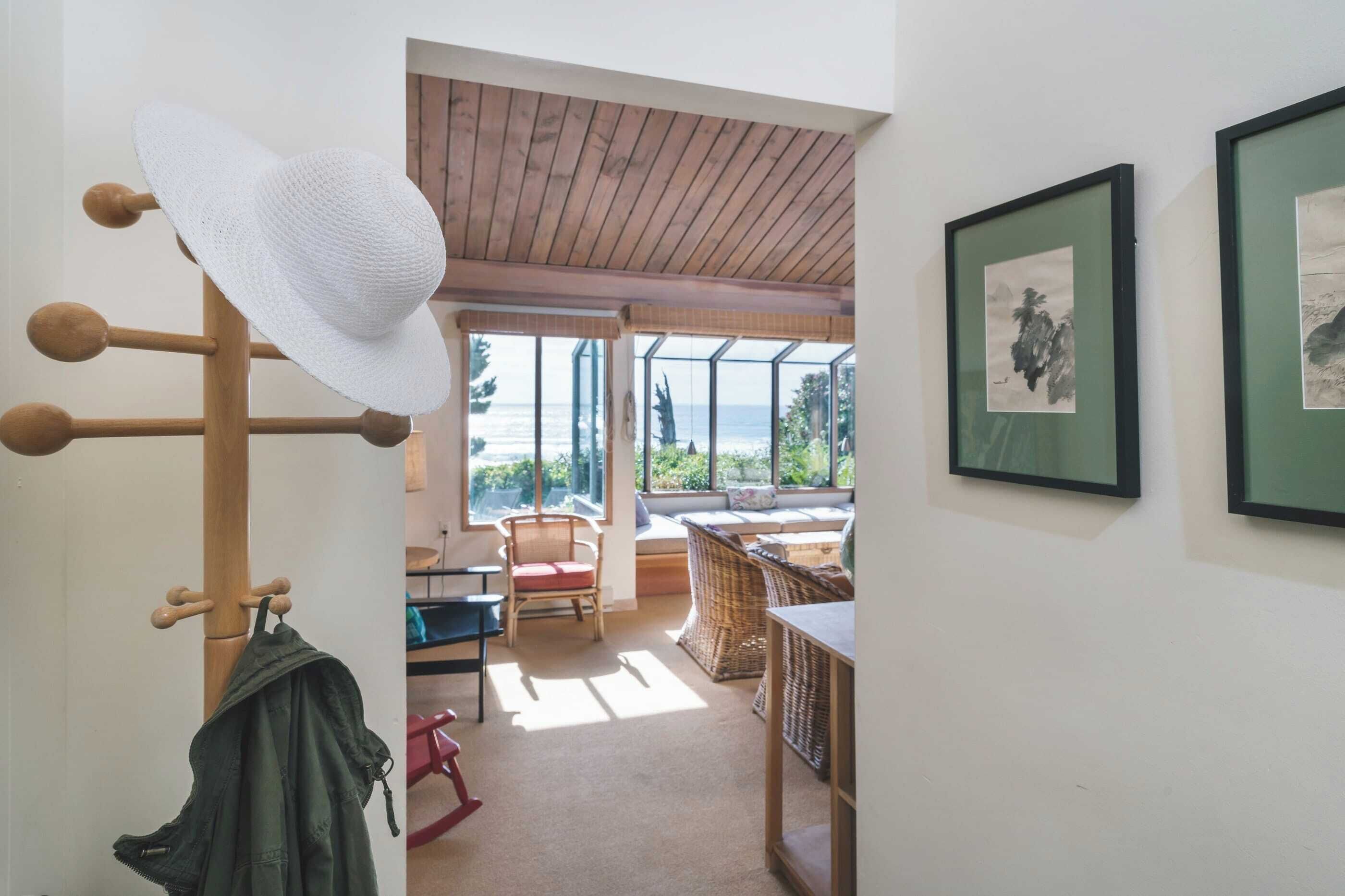 A room with a wooden ceiling, a large window with a view of the sea, a wicker chair, and a table.