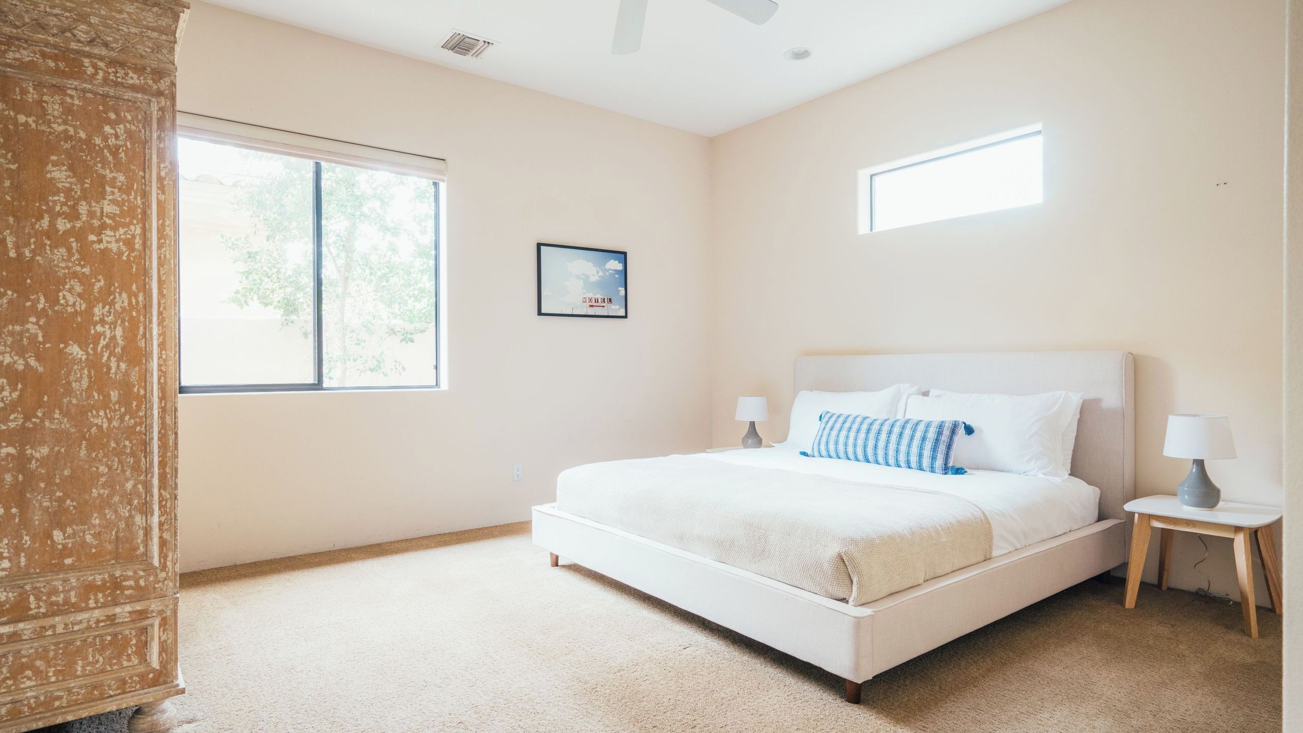 A bedroom with a bed, two bedside tables, a window, and a picture on the wall.