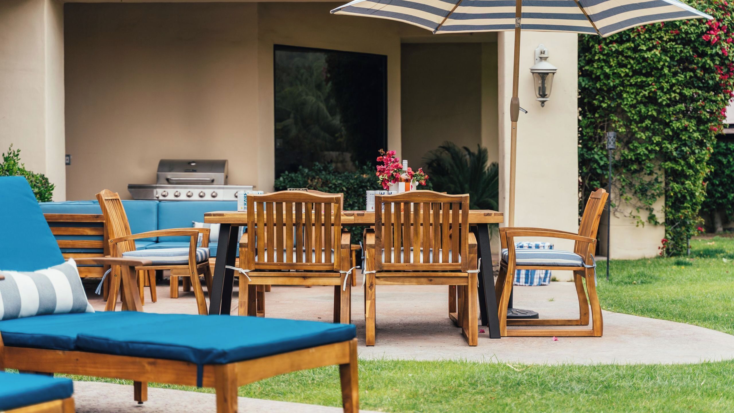 Une terrasse extérieure avec des meubles en bois, un barbecue et un grand parasol.