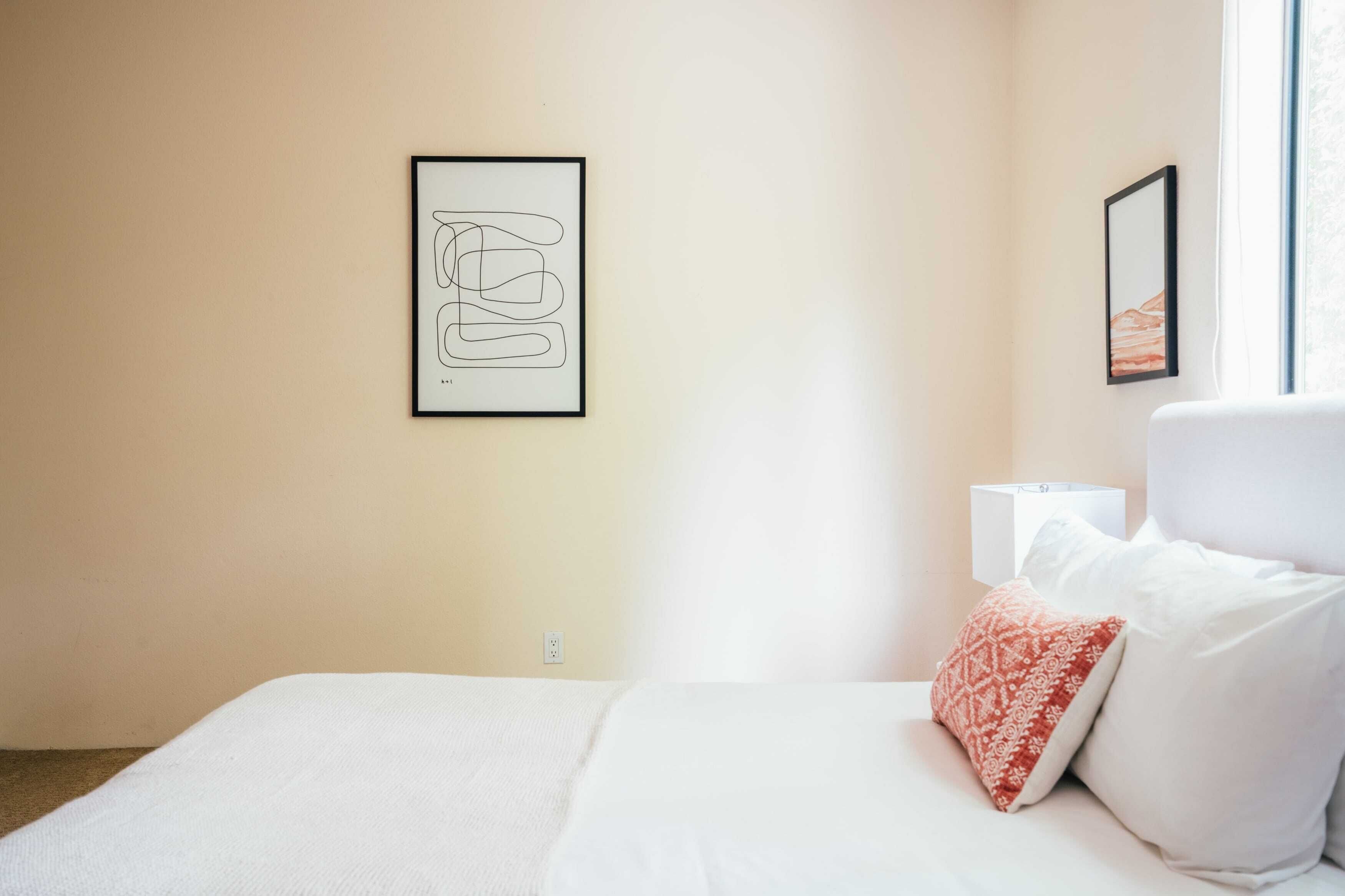 A hotel room with a bed, a bedside table, a lamp, and two framed pictures on the wall.