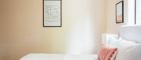 A hotel room with a bed, a bedside table, a lamp, and two framed pictures on the wall.