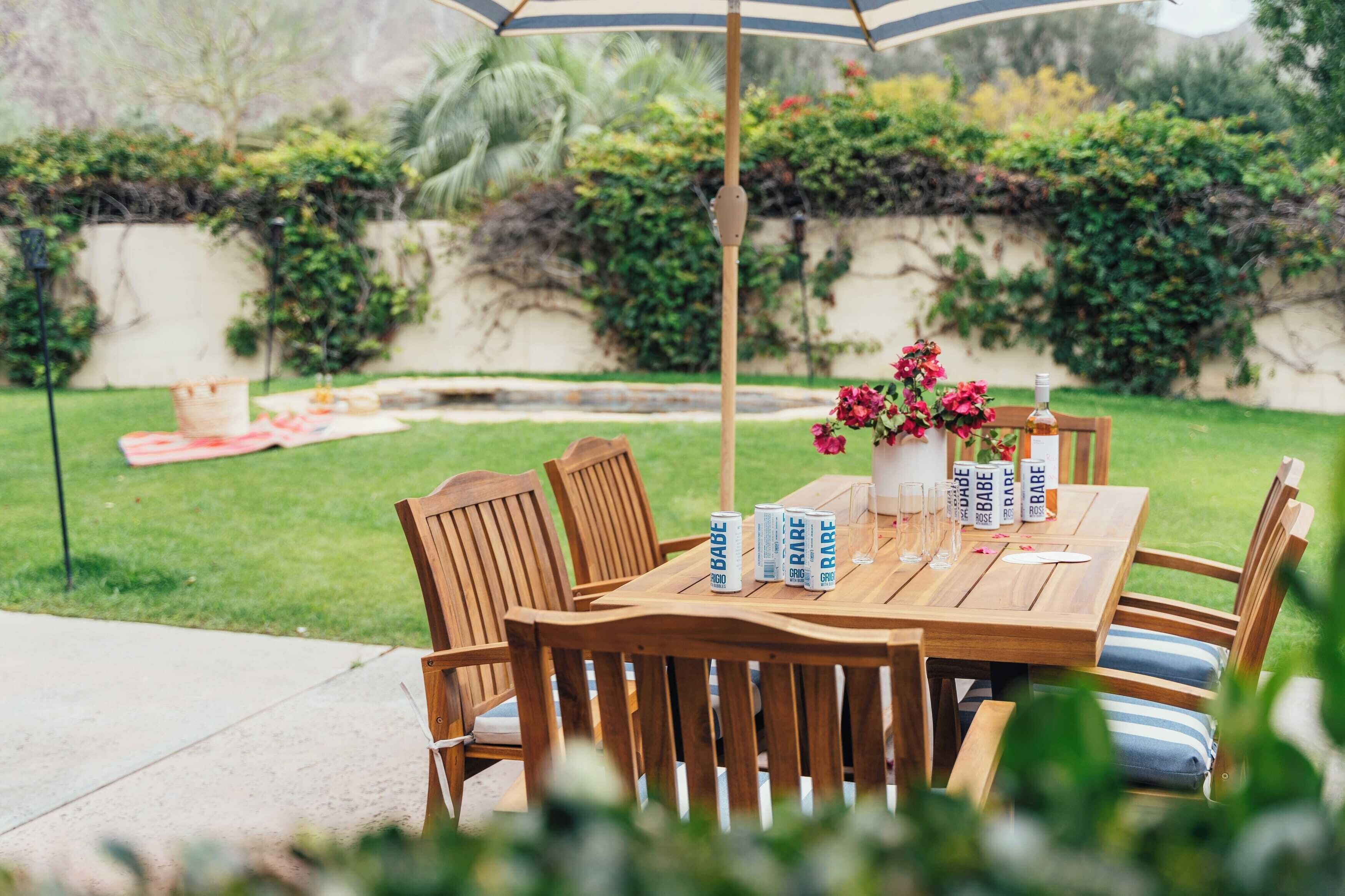 Una mesa de madera al aire libre con sillas, un paraguas a rayas y un florero con flores.