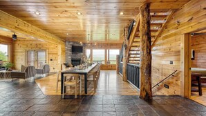 A spacious wooden cabin interior with a stone fireplace, a dining area, and a staircase. - Pine Rise by Avantstay10mins to Pigeon Forge! (Sevierville)