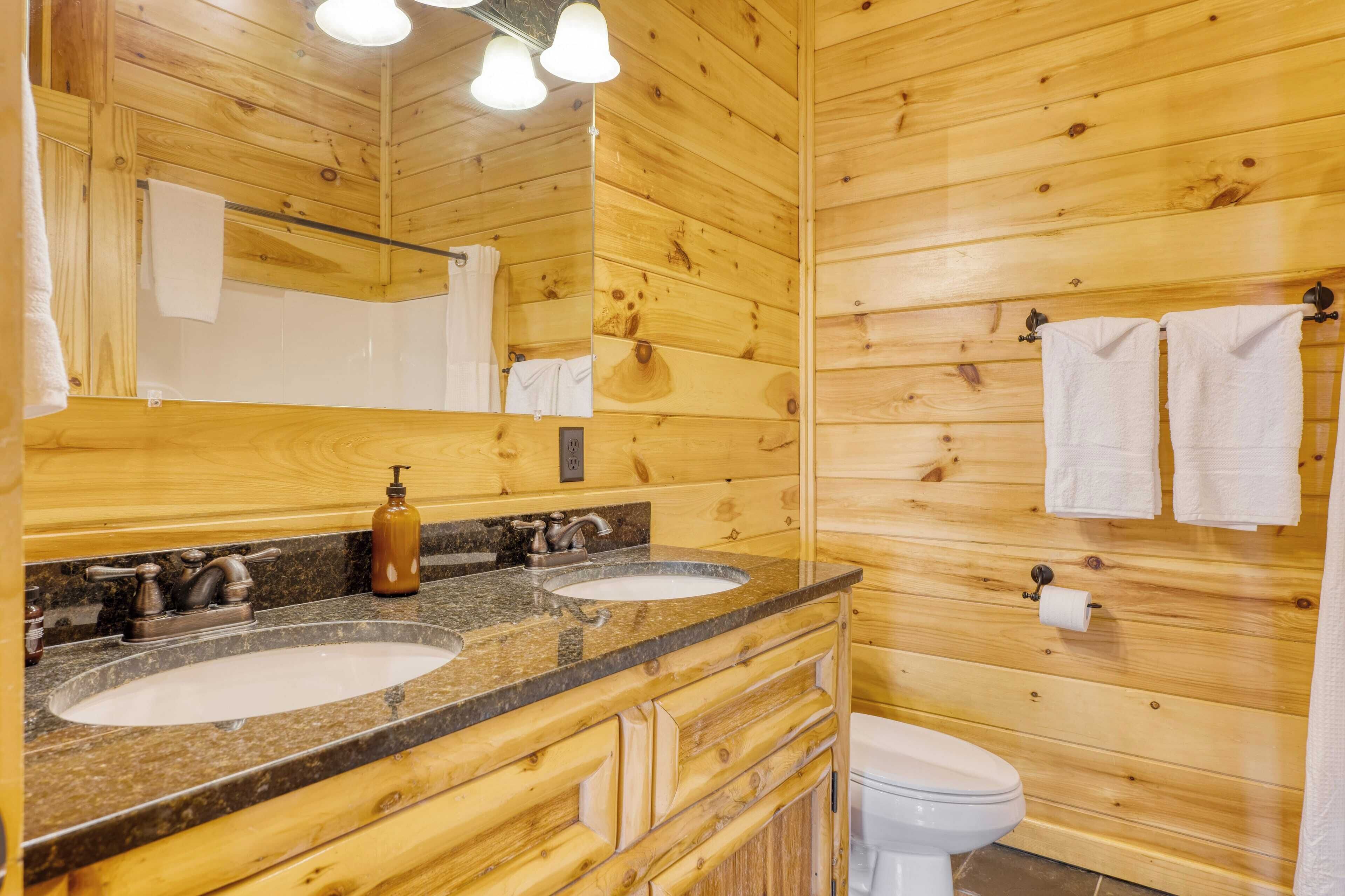 A wooden cabin bathroom with two sinks, a mirror, and a toilet.