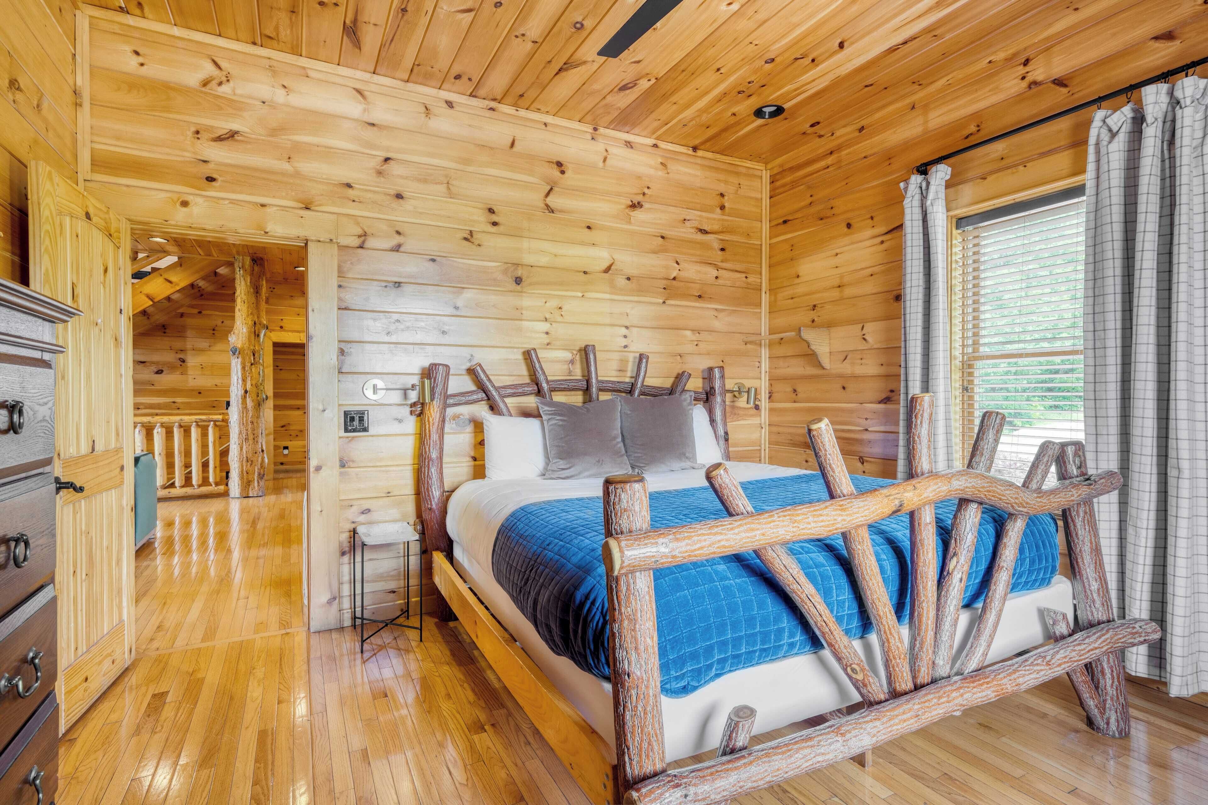 A wooden cabin bedroom with a bed, wooden headboard, and a view of the outdoors through a window.