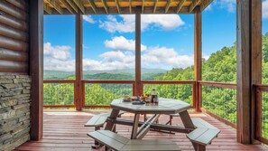 Um deck de madeira com uma mesa de piquenique e bancos, com vista para uma paisagem montanhosa.