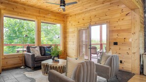 A cozy cabin interior with a wooden ceiling, a sofa, armchairs, a coffee table, and large windows offering a view of greenery. - Pine Rise by Avantstay10mins to Pigeon Forge! (Sevierville)