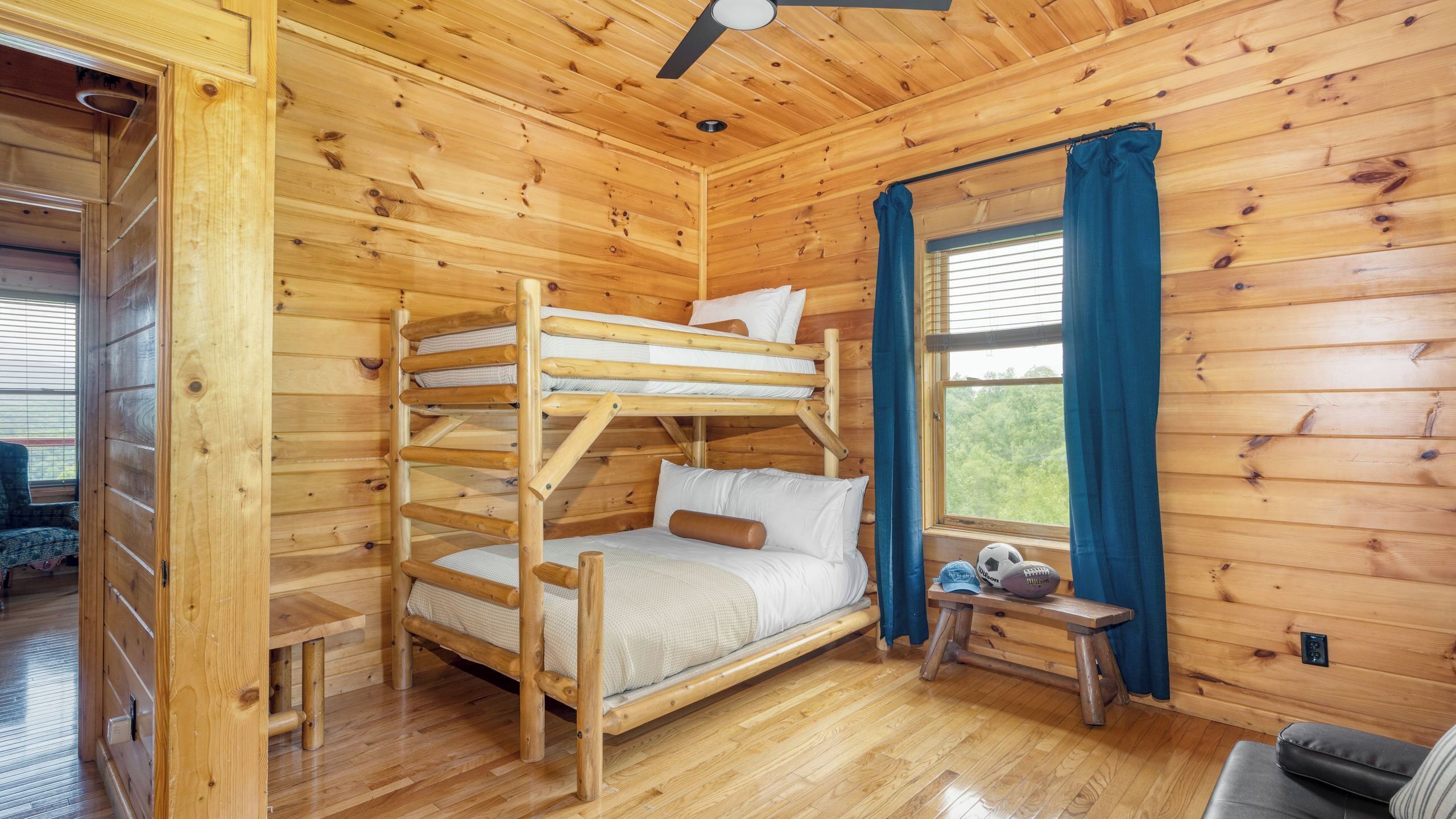 A wooden cabin with a bunk bed, a small table, a bench, and a window with curtains.