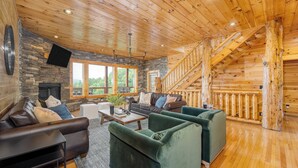 A log cabin interior with a stone fireplace, leather sofas, a dining table, and a staircase. - Pine Rise by Avantstay10mins to Pigeon Forge! (Sevierville)
