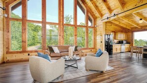 A spacious wooden cabin with large windows, a cozy living area with a sofa and chairs, a kitchen with wooden cabinets, and a refrigerator. - Pine Rise by Avantstay10mins to Pigeon Forge! (Sevierville)