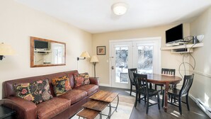 A living room with a brown leather sofa, a wooden coffee table, a dining table with chairs, a television mounted on the wall, and a door leading outside. - Viking Lodge 117 by Avantstay Ski Home, Near Town Park & Downtown (Telluride)