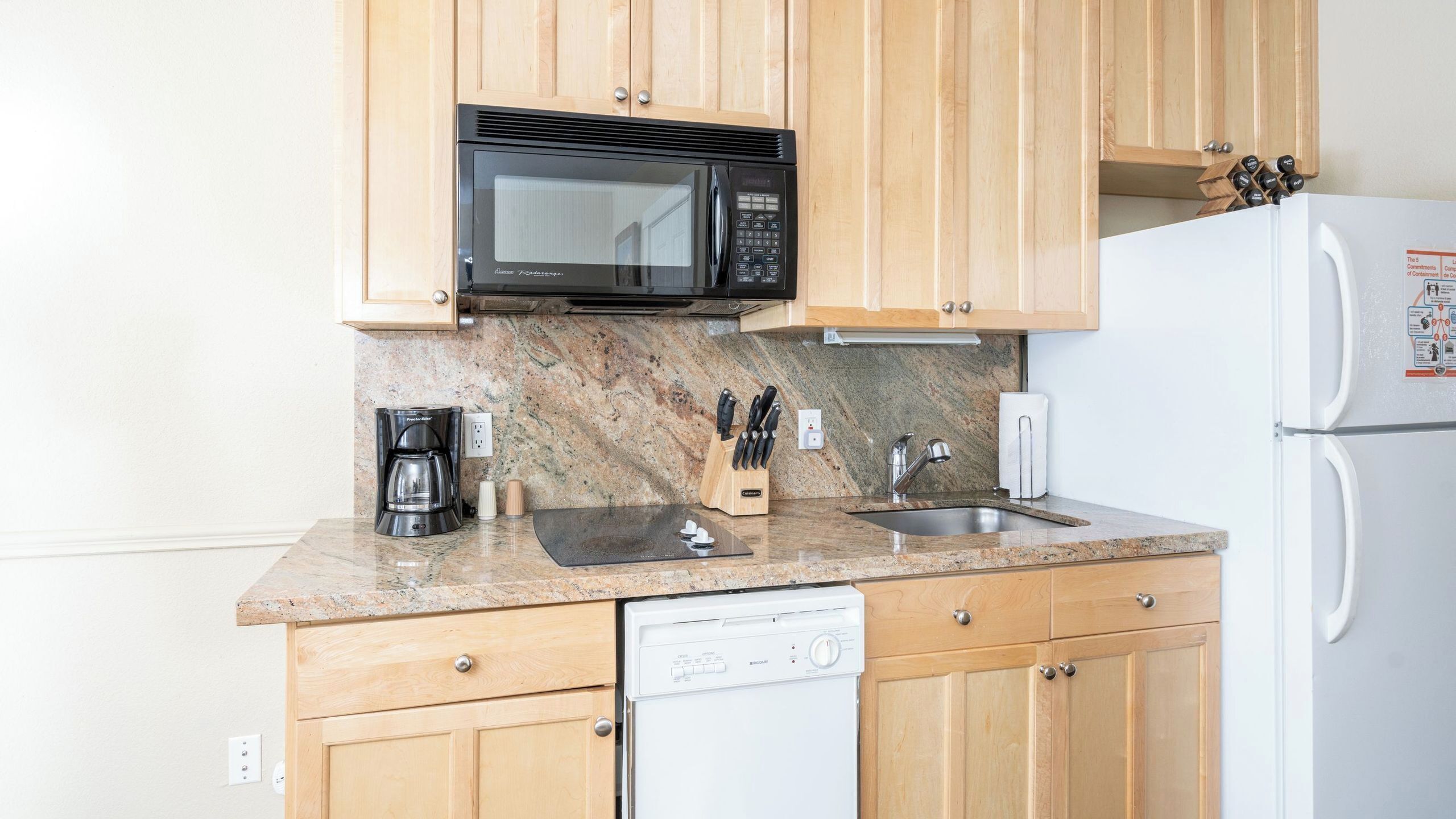 A kitchen with wooden cabinets, a microwave, a coffee maker, a sink, and a dishwasher.