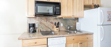 A kitchen with wooden cabinets, a microwave, a coffee maker, a sink, and a dishwasher.