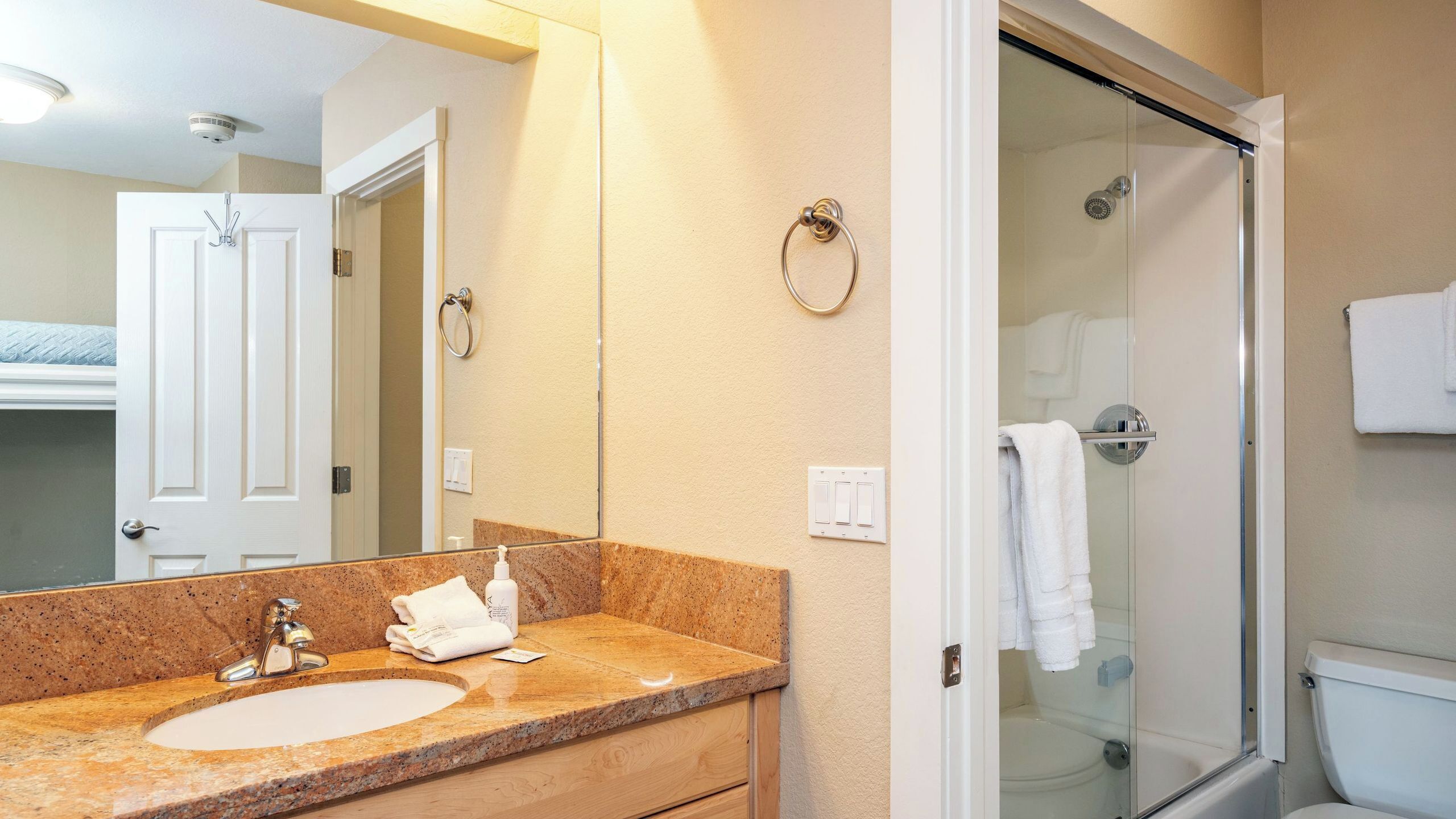 A bathroom with a sink, mirror, towel rack, and a glass shower enclosure.