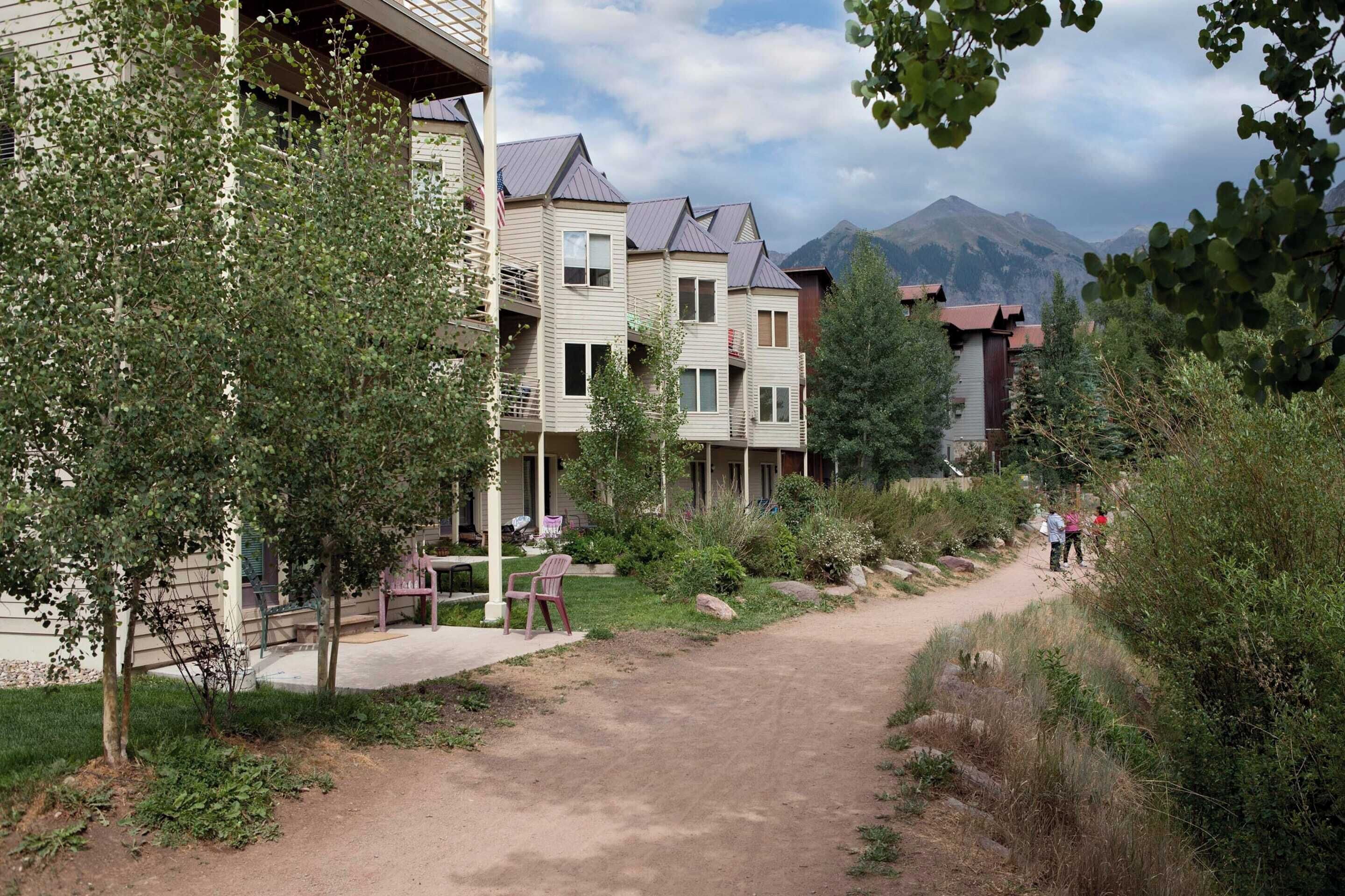 Um bairro residencial com vários edifícios de dois andares, um caminho de terra e vegetação.